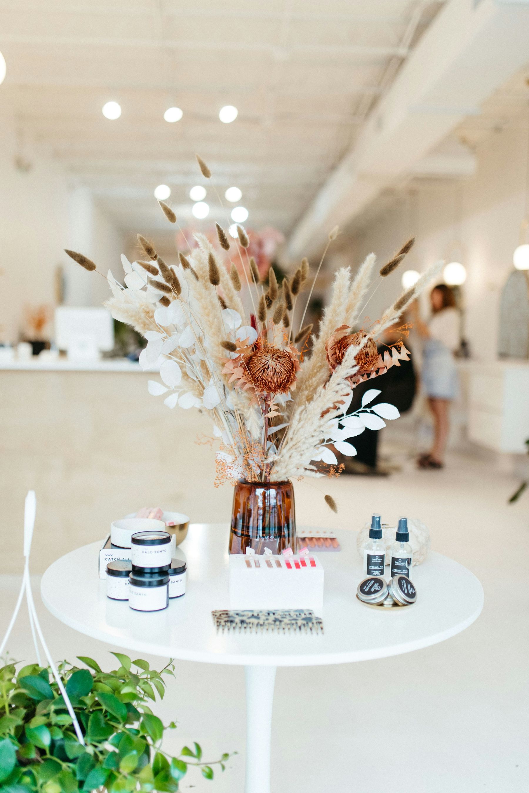 Bouquet de fleurs séchées et produits de soin sur une table blanche, à l’entrée du salon