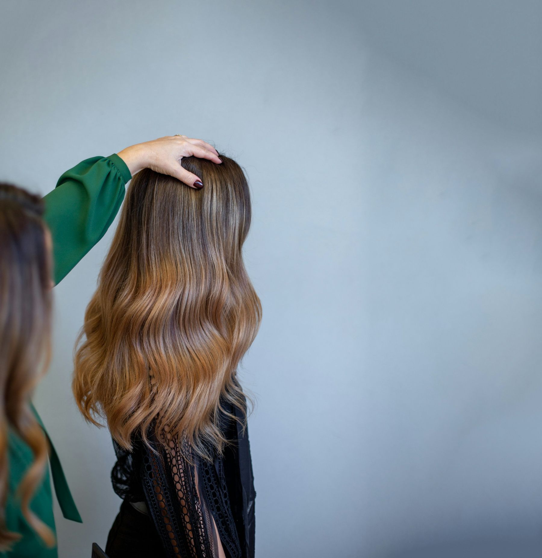 Une coiffeuse ajuste de longs cheveux ondulés au dégradé caramel