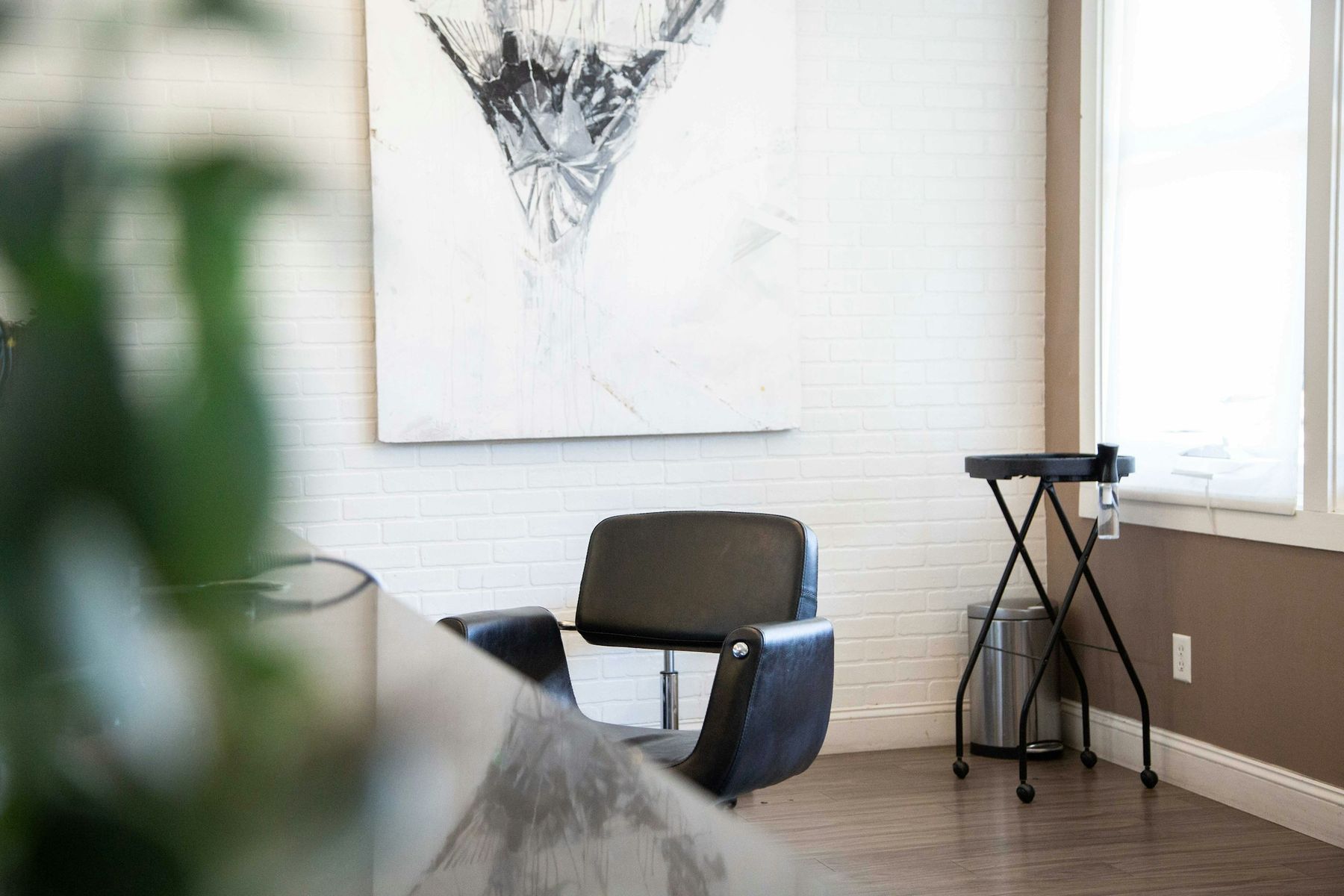 Fauteuil de coiffure noir devant un mur de briques blanches, près d’une fenêtre