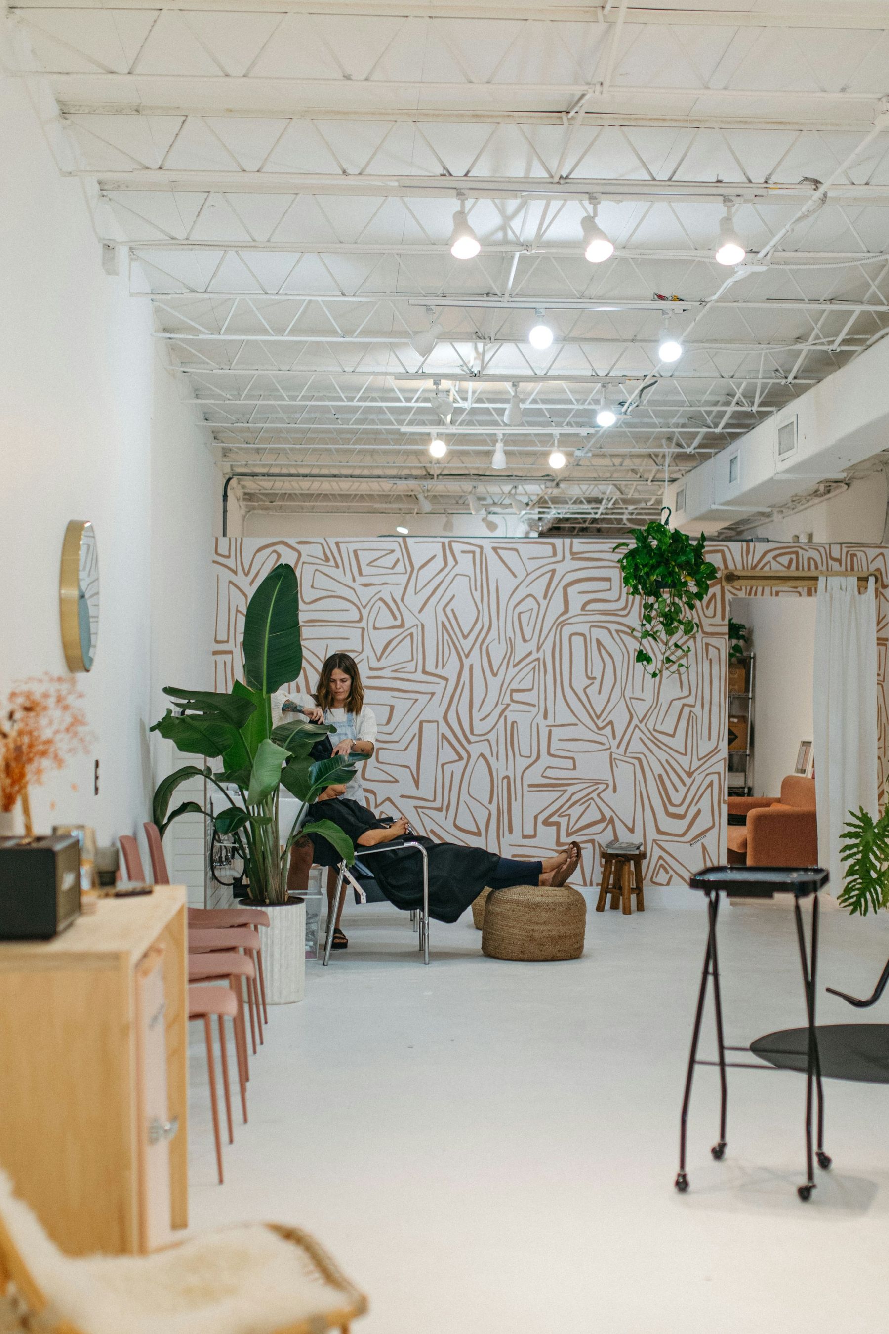 Le salon : une coiffeuse au travail entre les plantes, devant un mur peint de motifs